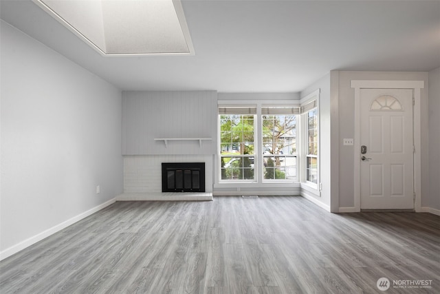 unfurnished living room with a brick fireplace, visible vents, baseboards, and wood finished floors