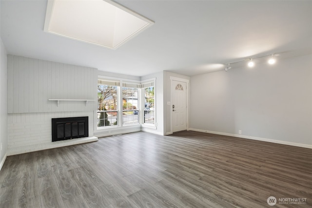 unfurnished living room with a brick fireplace, baseboards, wood finished floors, and rail lighting