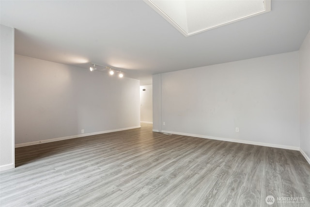 spare room featuring light wood-type flooring, baseboards, and track lighting