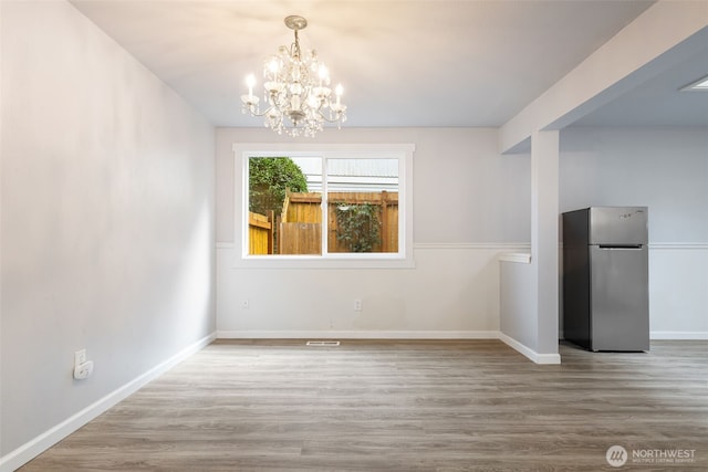 unfurnished dining area with a chandelier, wood finished floors, visible vents, and baseboards