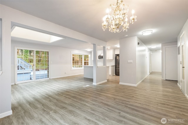 unfurnished living room with baseboards, light wood finished floors, and an inviting chandelier