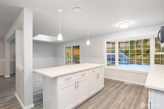 kitchen featuring white cabinets, a center island, decorative light fixtures, light countertops, and light wood-style floors