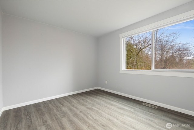 empty room with baseboards, visible vents, and wood finished floors