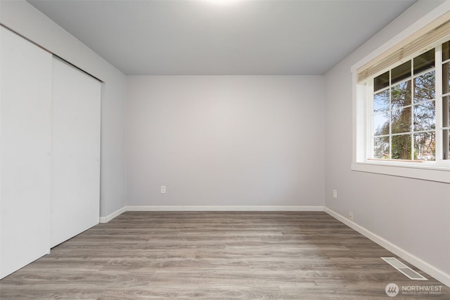 unfurnished bedroom featuring baseboards, a closet, visible vents, and wood finished floors