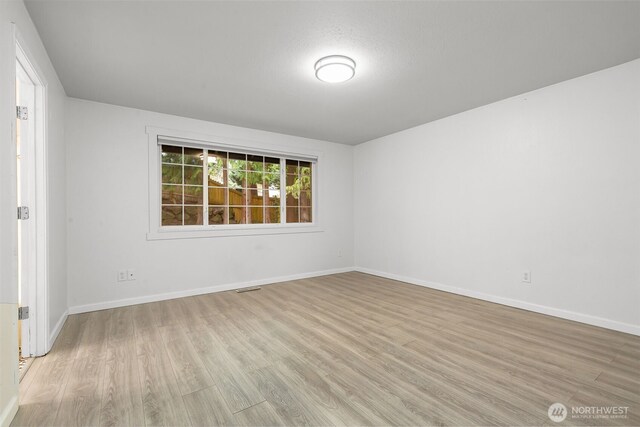 empty room featuring wood finished floors, visible vents, and baseboards