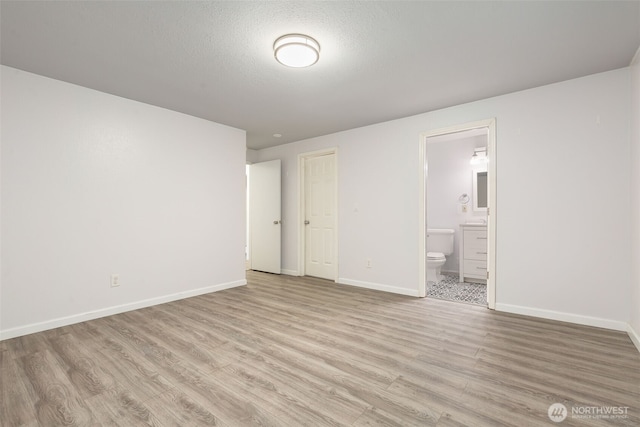 unfurnished bedroom featuring light wood-type flooring, ensuite bath, baseboards, and a textured ceiling