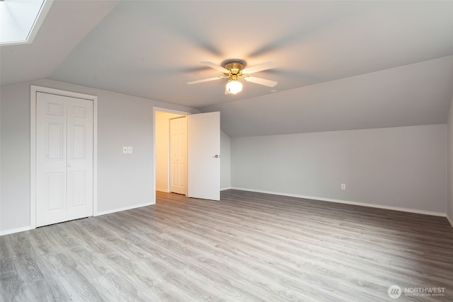 bonus room with vaulted ceiling with skylight, ceiling fan, baseboards, and wood finished floors