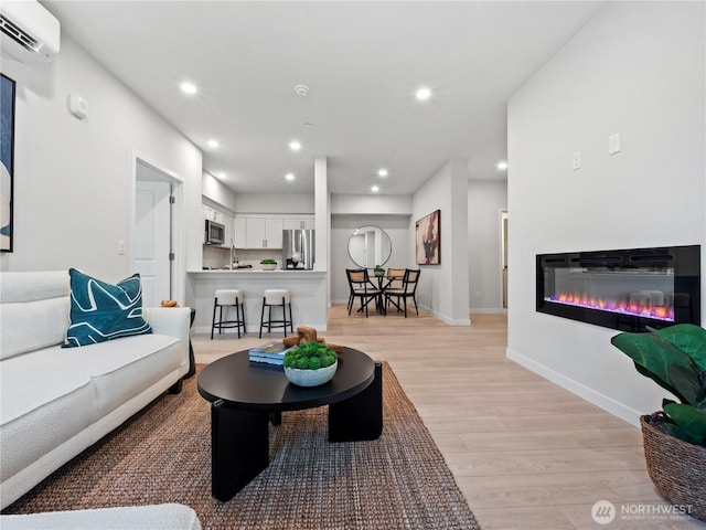 living room featuring recessed lighting, a wall mounted AC, light wood-style floors, a glass covered fireplace, and baseboards