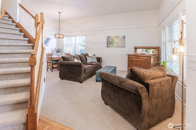 living area featuring carpet flooring, a healthy amount of sunlight, stairs, and a decorative wall