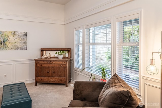 living area featuring a decorative wall, plenty of natural light, light colored carpet, and a wainscoted wall