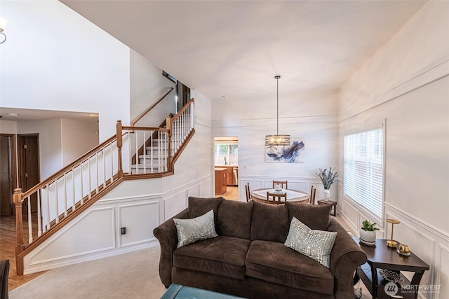 living room with a wainscoted wall, light carpet, a decorative wall, a chandelier, and stairs