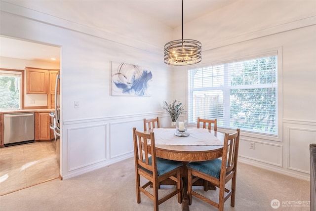 dining area featuring light carpet, a decorative wall, a chandelier, and a wainscoted wall