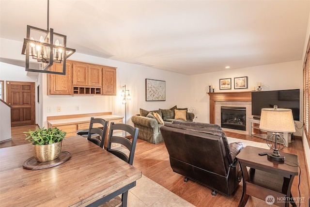 living room with a tiled fireplace, light wood-style flooring, and an inviting chandelier