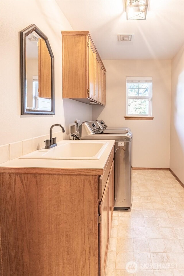 laundry room with washing machine and clothes dryer, visible vents, baseboards, cabinet space, and a sink