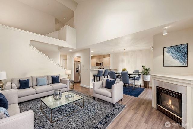 living room featuring light wood-style flooring, a fireplace, high vaulted ceiling, and baseboards