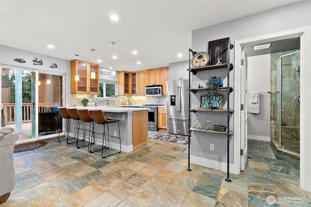 kitchen featuring a peninsula, appliances with stainless steel finishes, backsplash, a kitchen bar, and glass insert cabinets