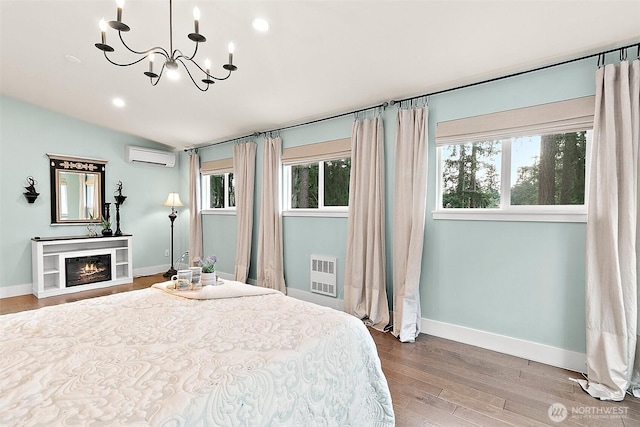 bedroom featuring lofted ceiling, a notable chandelier, wood finished floors, a wall mounted air conditioner, and a glass covered fireplace