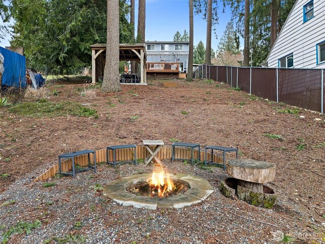 view of yard featuring a wooden deck, fence, a fire pit, and a gazebo