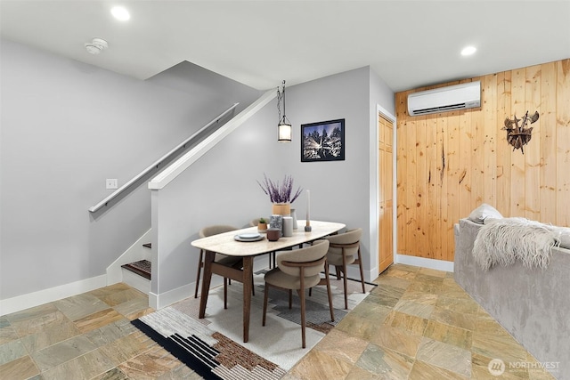 dining space featuring stairway, stone finish flooring, wooden walls, and a wall mounted AC