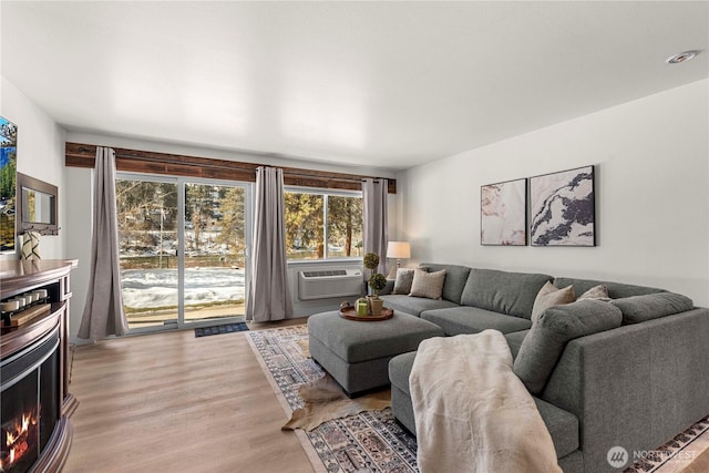 living room with a lit fireplace, cooling unit, and wood finished floors