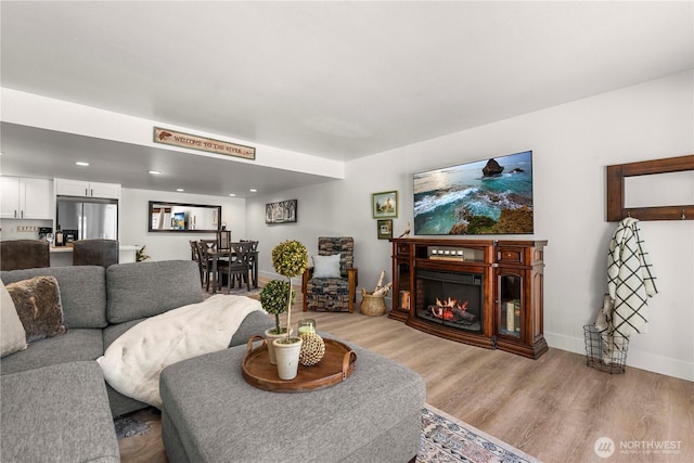 living area featuring baseboards, recessed lighting, a glass covered fireplace, and light wood-style floors