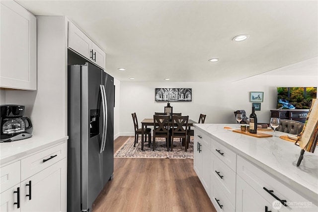 kitchen with recessed lighting, light stone countertops, white cabinets, wood finished floors, and stainless steel fridge