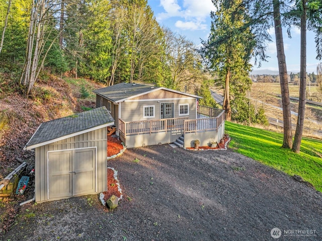 exterior space featuring an outdoor structure, board and batten siding, a deck, driveway, and a front lawn