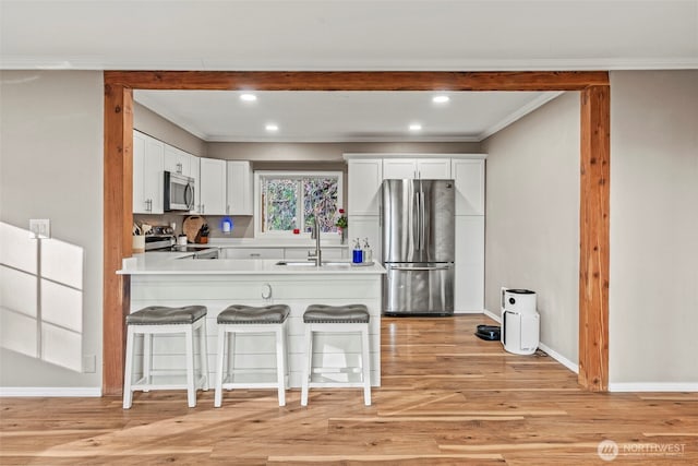 kitchen with stainless steel appliances, a sink, white cabinetry, a kitchen breakfast bar, and light countertops