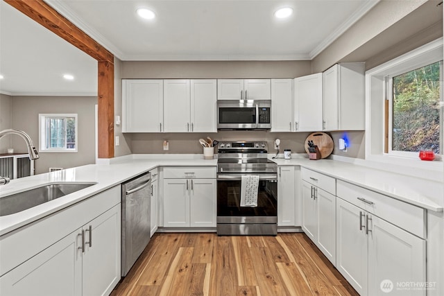 kitchen featuring appliances with stainless steel finishes, light countertops, crown molding, white cabinetry, and a sink