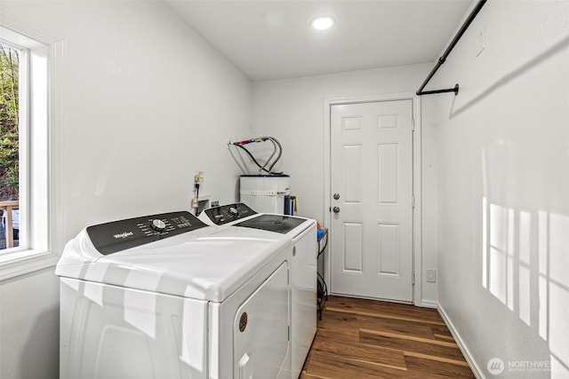 clothes washing area with laundry area, baseboards, secured water heater, dark wood-type flooring, and washing machine and clothes dryer