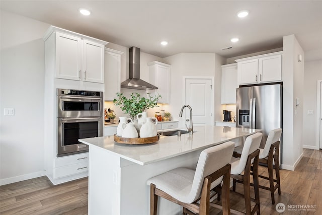 kitchen with stainless steel appliances, light countertops, white cabinets, a sink, and wall chimney range hood