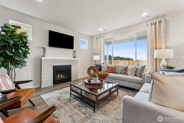 living room featuring light wood-type flooring, a glass covered fireplace, visible vents, and baseboards