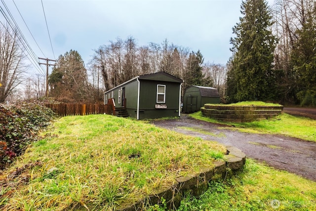 view of property exterior with driveway, a storage unit, an outdoor structure, and fence