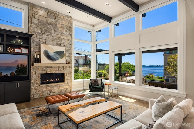 sunroom with beam ceiling, a water view, and a fireplace