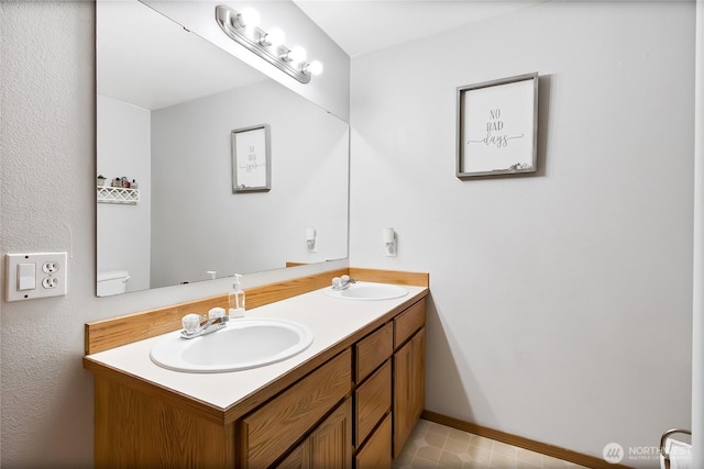 full bathroom with double vanity, baseboards, toilet, and a sink