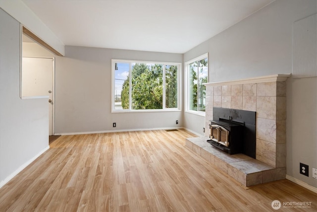 unfurnished living room with a wood stove, baseboards, visible vents, and light wood finished floors