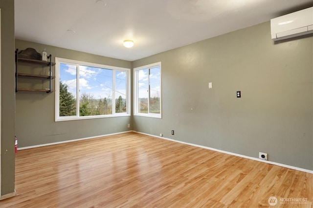 spare room featuring a wall mounted air conditioner, light wood-style flooring, and baseboards