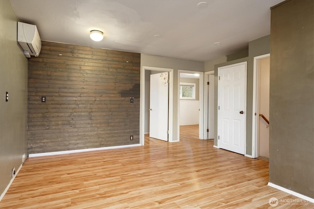 empty room with light wood-type flooring, baseboards, and a wall mounted AC