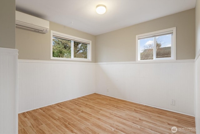 spare room featuring a wainscoted wall, light wood finished floors, and a wall unit AC