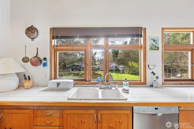 kitchen with dishwasher, a sink, tile counters, and brown cabinets