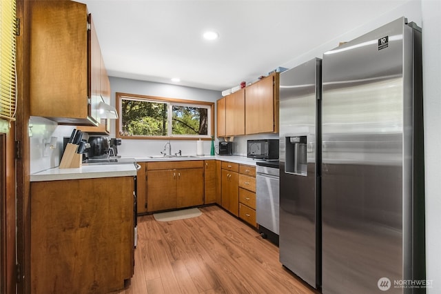 kitchen with light countertops, appliances with stainless steel finishes, a sink, and brown cabinets