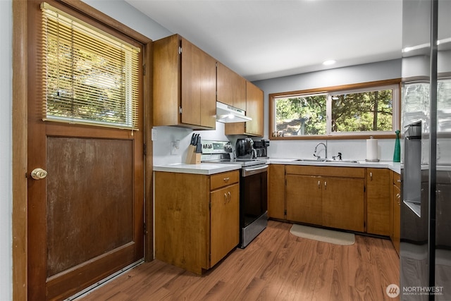 kitchen featuring electric stove, light wood-style flooring, light countertops, under cabinet range hood, and a sink