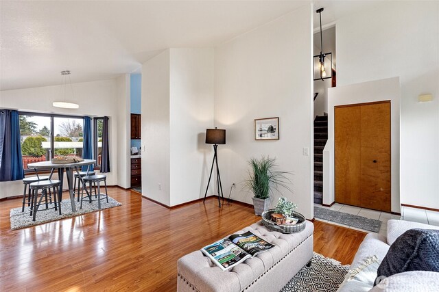 living room featuring high vaulted ceiling, stairs, baseboards, and wood finished floors