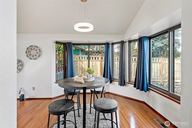 dining area with a wealth of natural light, visible vents, lofted ceiling, and wood finished floors