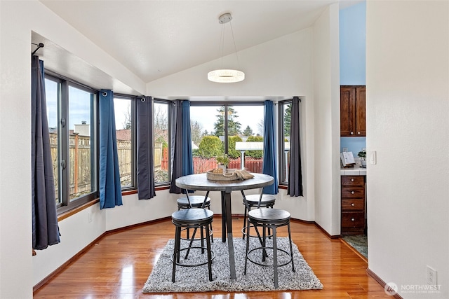 dining room with baseboards, light wood-type flooring, and lofted ceiling