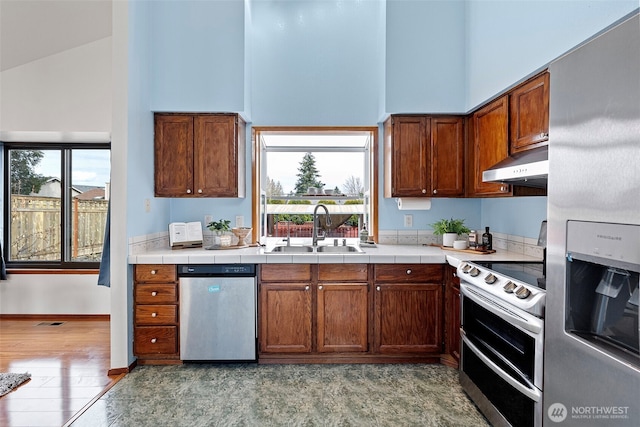 kitchen with under cabinet range hood, high vaulted ceiling, appliances with stainless steel finishes, and a sink