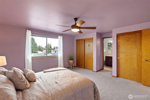 bedroom with a textured ceiling, light colored carpet, two closets, and ceiling fan