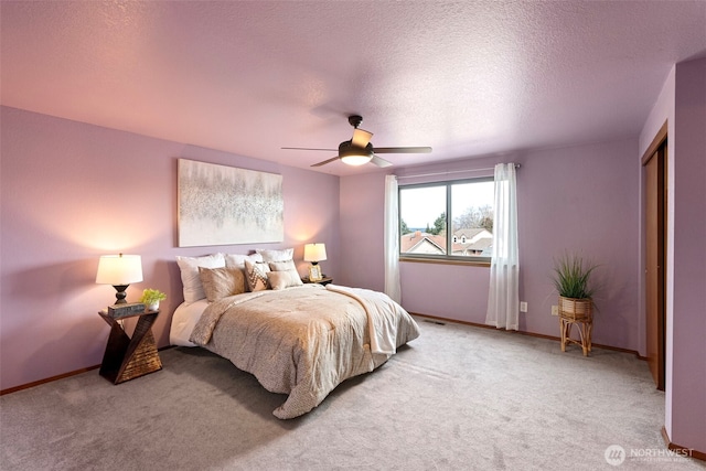 bedroom with baseboards, light colored carpet, a ceiling fan, and a textured ceiling