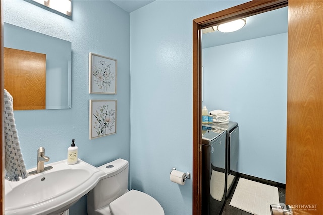 half bathroom featuring toilet, separate washer and dryer, and a sink