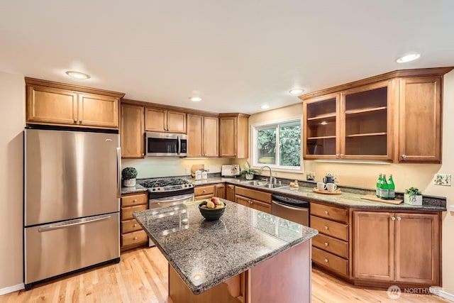 kitchen featuring stainless steel appliances, light wood-style floors, glass insert cabinets, a sink, and a kitchen island